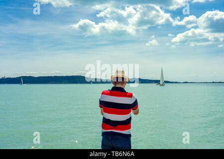 L'uomo guarda velieri dalla costa al Lago Balaton Ungheria in una giornata di sole Foto Stock