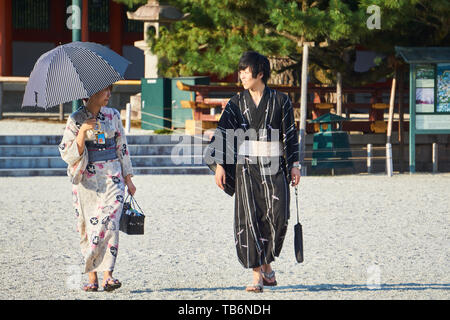 Un turista giapponese giovane vestito in tradizionale kimono yukata guardarsi reciprocamente in Heian Jingu's courtyard. La donna tiene un ombrello. Foto Stock