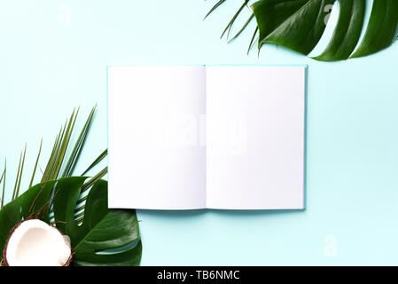 Green monstera, foglie di palma, di cocco, di notebook su sfondo rosa. Femmina scrittore blog workspace, torna al concetto di scuola. Lay piatto. Vista superiore Foto Stock