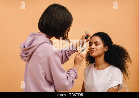 Parrucchiere professionista corregge il trucco durante il servizio fotografico Foto Stock