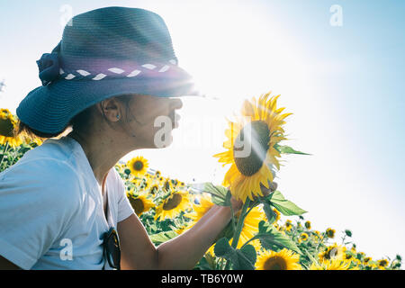 Donna con cappello baciare una pianta di girasole Foto Stock