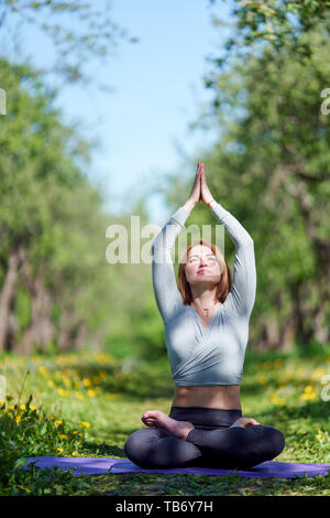 Immagine della ragazza giovane fare yoga seduti nella posizione del loto sul tappeto blu nei boschi di giorno di estate Foto Stock