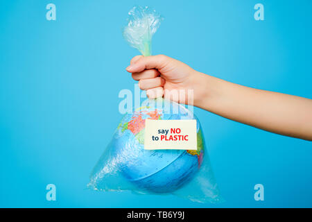 La donna tiene in mano una busta di plastica e del pianeta terra con etichetta di testo-DIRE NO ALLA PLASTICA a sfondo blu. Il concetto di inquinamento in plastica. Foto Stock