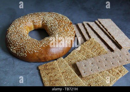 Un bagel freschi con i semi di sesamo. Nelle vicinanze sono sottili fette biscottate. Sfondo vintage. Una sana colazione gustosa. Foto Stock