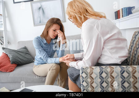 Donna di mezza età psychologyst terapia con client presso l ufficio seduta tenendo la mano mentre la sorella di piangere lacrime di tergitura via triste Foto Stock
