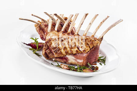 Gourmet rack arrosto di agnello condite con rosmarino e spicchi di aglio e servita con cipolla rossa su uno sfondo bianco per la pubblicità o il menu Foto Stock