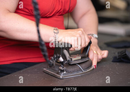 Close up di un irriconoscibile adattare la stiratura di panni con vecchio ferro metallico in un tradizionale atelier studio . Foto Stock