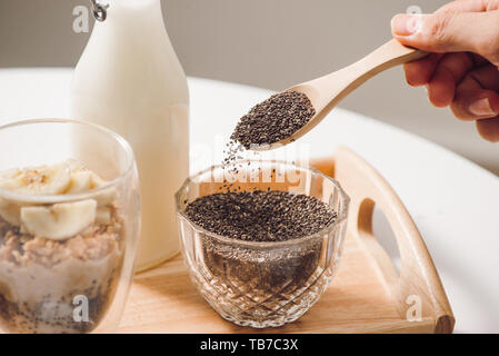 Pronto a mangiare sano una nutriente colazione - granola con mandorle e semi di Chia, banana e kiwi frutti e bacche e un vaso con latte nelle vicinanze Foto Stock