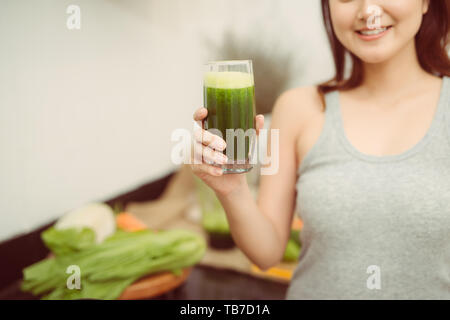 Piuttosto giovane donna bere un frullato vegetale nella sua cucina Foto Stock