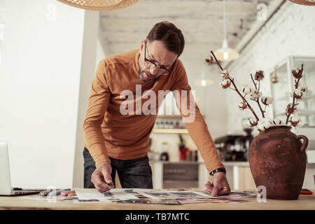 Tenendo un dibattito con te stesso. Riflessivo designer di moda la piegatura sul suo tavolo con bozzetti profondo nel suo lavoro. Foto Stock