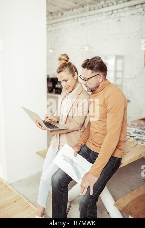 Ricerca di idee. Fashion designer che lavora per la sua nuova collezione con il suo assistente intelligente guardando il laptop. Foto Stock