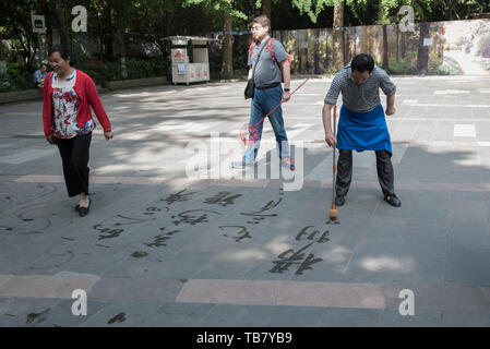 Elerly uomini cinesi la pratica di calligrafia sul terreno al Parco Huanhua, Chengdu Sichuan, Cina Foto Stock