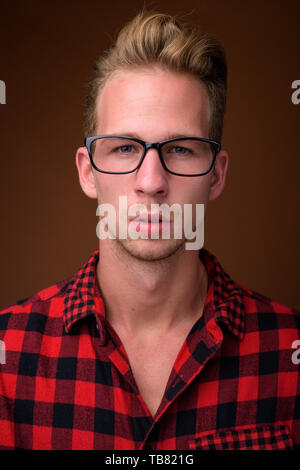 Studio shot del giovane uomo bello indossare rosso camicia a scacchi contro sfondo marrone Foto Stock