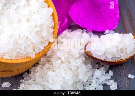 Bagno bianco sale in una ciotola di legno con un cucchiaio e un'orchidea sul tavolo di legno Foto Stock