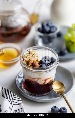 Farina di avena con mandorle noci, mirtillo, marmellata e yogurt in un barattolo di vetro sul tavolo per la colazione in mattina d'estate. Concetto di sano cibo gustoso. Foto Stock