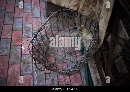 Vecchio cesto in vimini realizzato in maglia in alluminio su un pavimento piastrellato in un cortile rurale Foto Stock