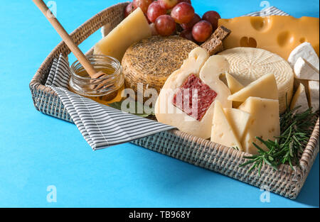 Vassoio di vimini con assortimento di formaggi saporiti sul colore di sfondo Foto Stock