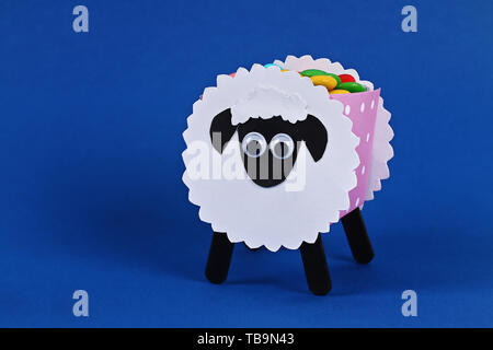 Fai da te l'Eid Al Adha agnello pecore caramella dolce carta, i bastoncini di legno per gelato su sfondo blu. Idea regalo, e il decor e l'Eid Al Adha. Procedimento kid bambini craft Foto Stock