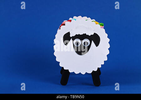 Fai da te l'Eid Al Adha agnello pecore caramella dolce carta, i bastoncini di legno per gelato su sfondo blu. Idea regalo, e il decor e l'Eid Al Adha. Procedimento kid bambini craft Foto Stock