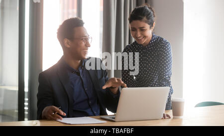 Multietnica sorridente diversi colleghi parlare cooperante al laptop Foto Stock
