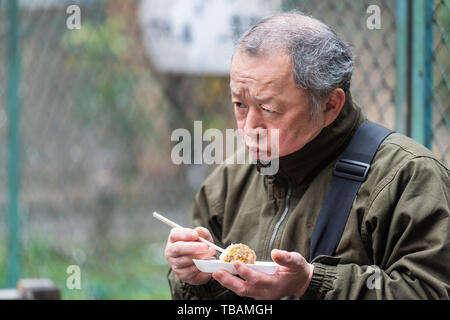 Tokyo, Giappone - 30 Marzo 2019: mercato esterno street di Tsukiji vicino a Ginza con uomo piastra di contenimento di cibo di riso mangiare a sfera Foto Stock