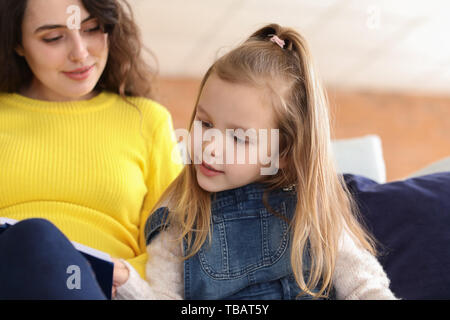 Donna incinta con piccola figlia libro di lettura a casa Foto Stock