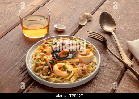 Piatti di pasta. Tagliolini con cozze, gamberi, vongole e anelli di totano, con un bicchiere di vino al buio su un rustico sfondo di legno Foto Stock