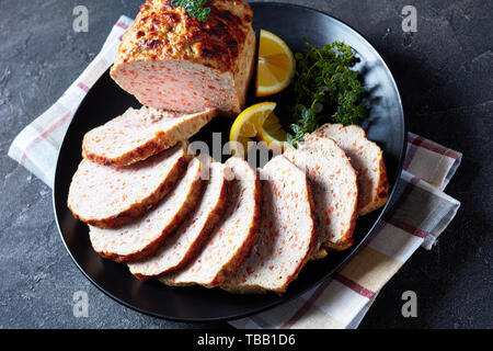 Close-up di fettine di polpettone di pollo servito su una piastra nera con le fette di limone e di timo fresco su una tavola di cemento, vista da sopra Foto Stock