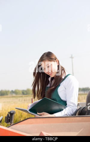 Giovane donna cinese agonomist in golden campo di cereali con piccole harvester Foto Stock