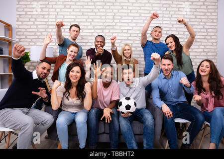 Emozionato multirazziale amici seduti sul divano guardando la partita di calcio a casa Foto Stock