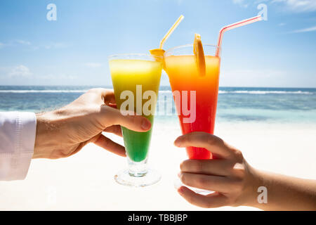 Close-up del giovane la mano tostare i colorati bicchieri da cocktail di fronte al mare in spiaggia Foto Stock