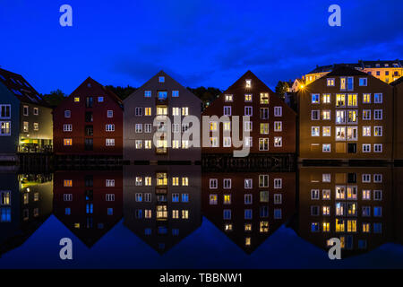 Tradizionale vecchi granai convertiti in edifici residenziali riflettente nel fiume Nidelva di notte, Trondheim, Norvegia Foto Stock