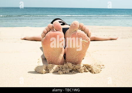 Close-up di una giovane donna sdraiata sulla sabbia con il suo confuso piedi sulla spiaggia Foto Stock