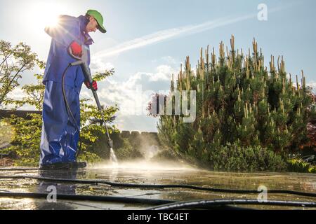 Pulizia di potenza utilizzando la rondella a pressione. Gli uomini di lavaggio i percorsi del giardino. Foto Stock