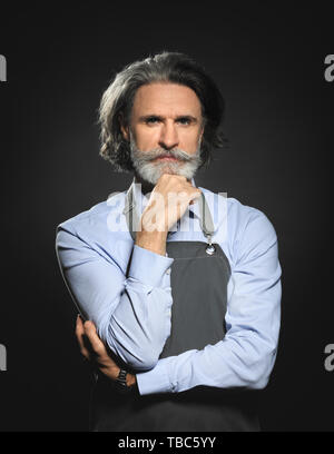 Senior uomo in grembiule su sfondo scuro Foto Stock