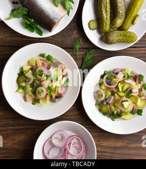 Insalata di pesce con le aringhe salate, patate bollite, cipolla, marinata di cetriolo e Apple su un tavolo di legno. Vista superiore, laici piatta Foto Stock