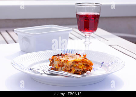 Fetta di lasagna su un piatto e un bicchiere di vino in una tabella Foto Stock