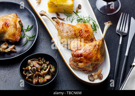 Gambe di Anatra confit con patate gratinate e fungo su una piastra. Close up. Foto Stock