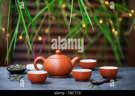 Il tè verde nella teiera e chawan bocce, tazze. Sfondo esterno con foglie di bambù e bokeh luci. Copia dello spazio. Foto Stock