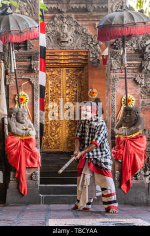 Banjar Gelulung, Bali, Indonesia - 26 Febbraio 2019: Mas villaggio. Riprodurre sul palco l'impostazione. Banditi con bastone danze vestito con il grigio-bianco a quadretti Foto Stock