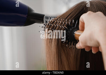 Parrucchiere con asciugacapelli spazzolare i capelli lunghi della giovane donna in salone, primo piano Foto Stock