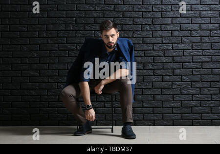 Moda giovane uomo seduto vicino a scuro muro di mattoni Foto Stock