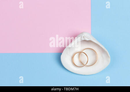 Gli anelli di nozze in bianco seashell sul pastello blu sfondo rosa, design minimalista, vista dall'alto lay piatto Foto Stock