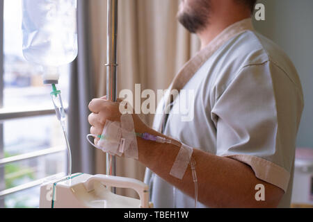 Close-up. paziente con un contagocce guarda fuori dalla finestra della stanza di ospedale e sorrisi. vista posteriore. Il concetto di assistenza sanitaria. Foto Stock