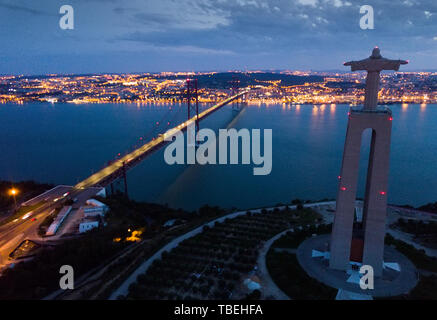 Notte Vista aerea da Almada del Santuario di Cristo Re e 25 de Abril ponte contro uno sfondo illuminato di Lisbona, Portogallo Foto Stock