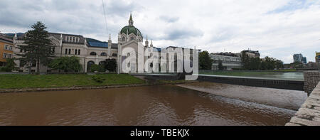 Sarajevo: il festina lente bridge con la sua looping in medio, oltre il fiume Miljacka e il palazzo dell'Accademia di Belle Arti, Università pubblica Foto Stock