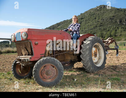 Esperti giovane donna alla guida di piccole trattore agricolo, la lavorazione del terreno sul suo orto Foto Stock