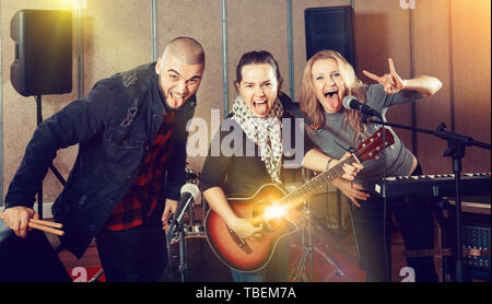 Tre compagni di band sorridente in posa insieme con gli strumenti musicali in sala prove Foto Stock