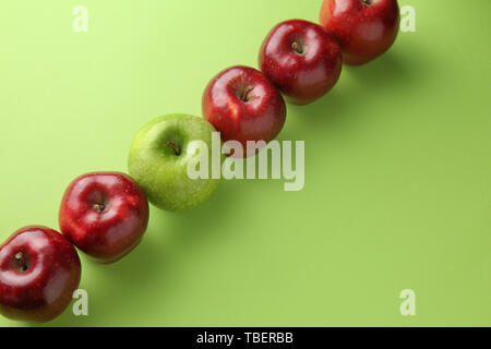 Green apple tra quelli rossi su sfondo colorato. Concetto di unicità Foto Stock