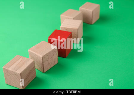 Il cubo rosso tra quelli di legno su uno sfondo colorato. Concetto di unicità Foto Stock